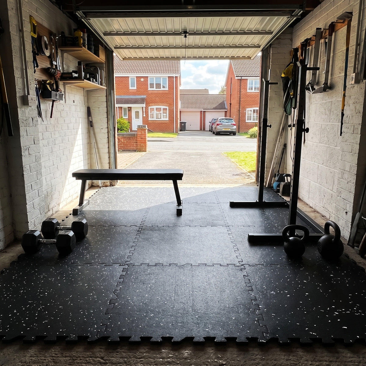 12mm white fleck interlocking rubber gym tiles laid on a concrete garage floor for a home gym with bench and dumbbells