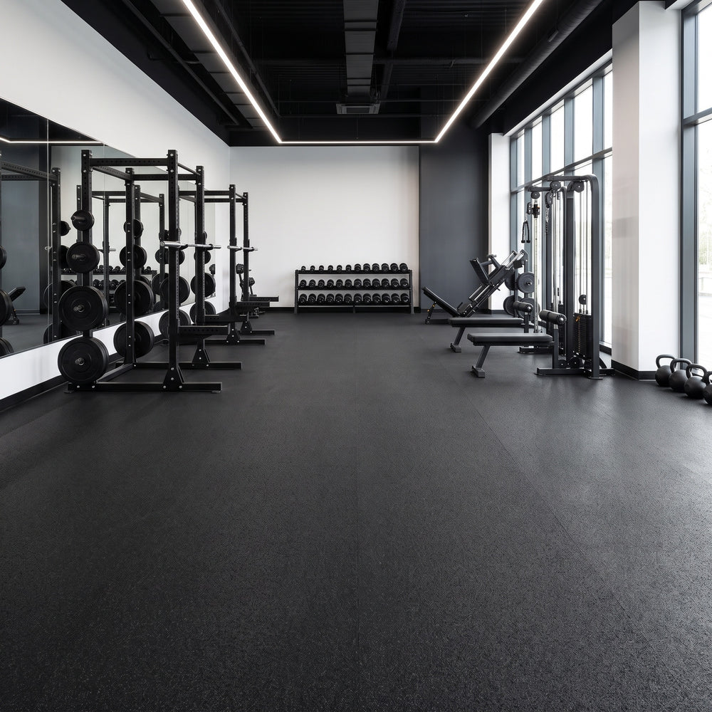 10m black rubber crumb gym flooring rolls laid with near-invisible joins across a professional commercial gym with power racks, dumbbells, leg press and cable machine