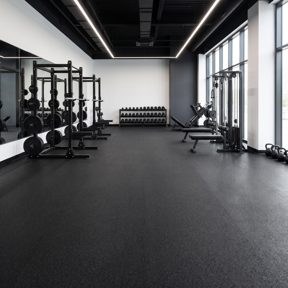 Black rubber gym flooring laid in long 1m-wide roll runs with near-invisible joins across a professional commercial gym with power racks, dumbbells, leg press and cable machine