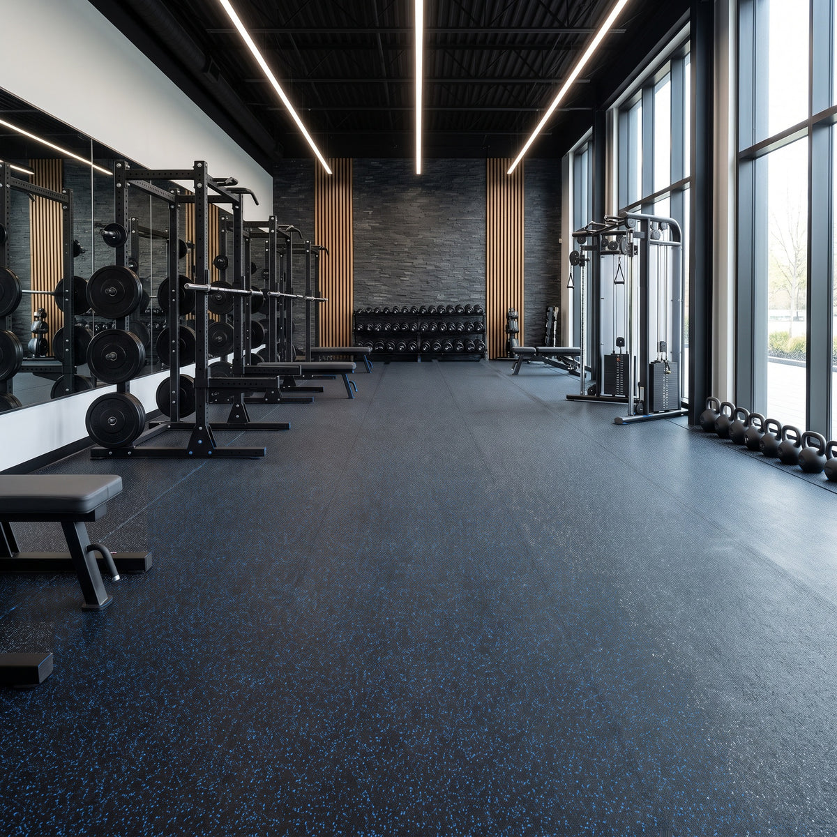 Black rubber gym flooring with blue fleck in long 1m-wide roll runs with near-invisible joins across a high-end commercial gym with power racks, dumbbells, cable crossover and kettlebells