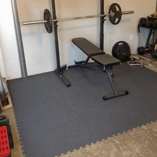 Customer photo: EVA foam gym tiles under a squat rack and bench in a home gym