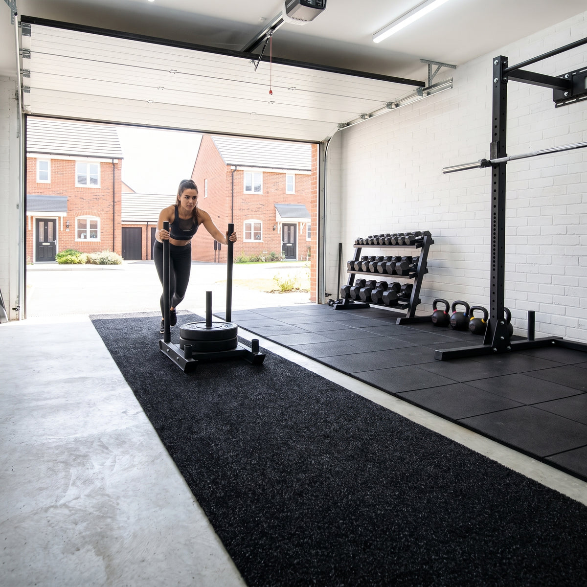 Black gym turf sled track in a garage gym next to rubber gym tiles